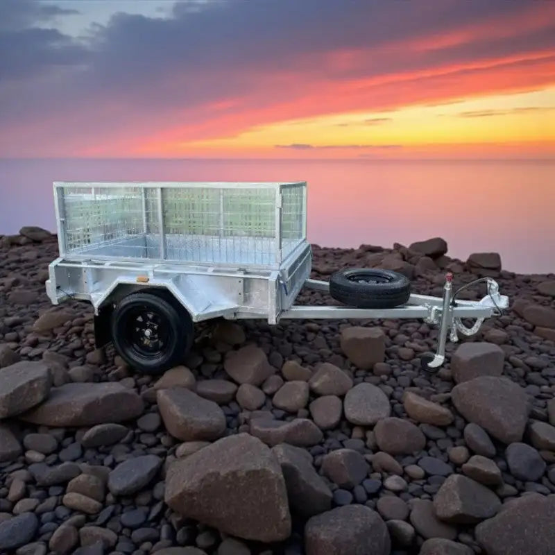 Silver aluminum utility trailer with a mesh-sided cargo bed and black tires, featuring a spare tire mounted on the side.